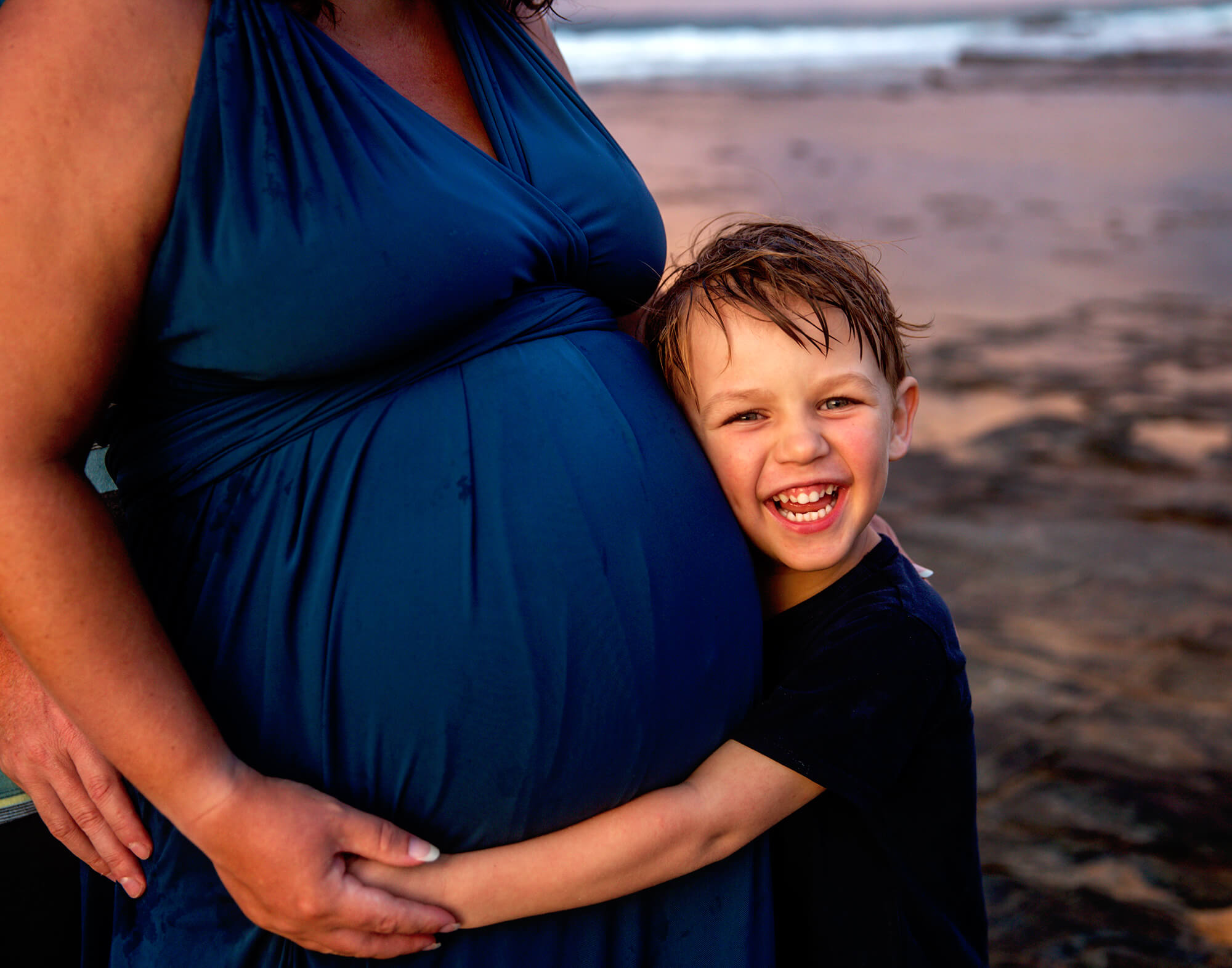 older brother cuddling his mothers pregnant belly waiting on his little brother rainbow baby rocks at point cartwright kawana sunshine coast