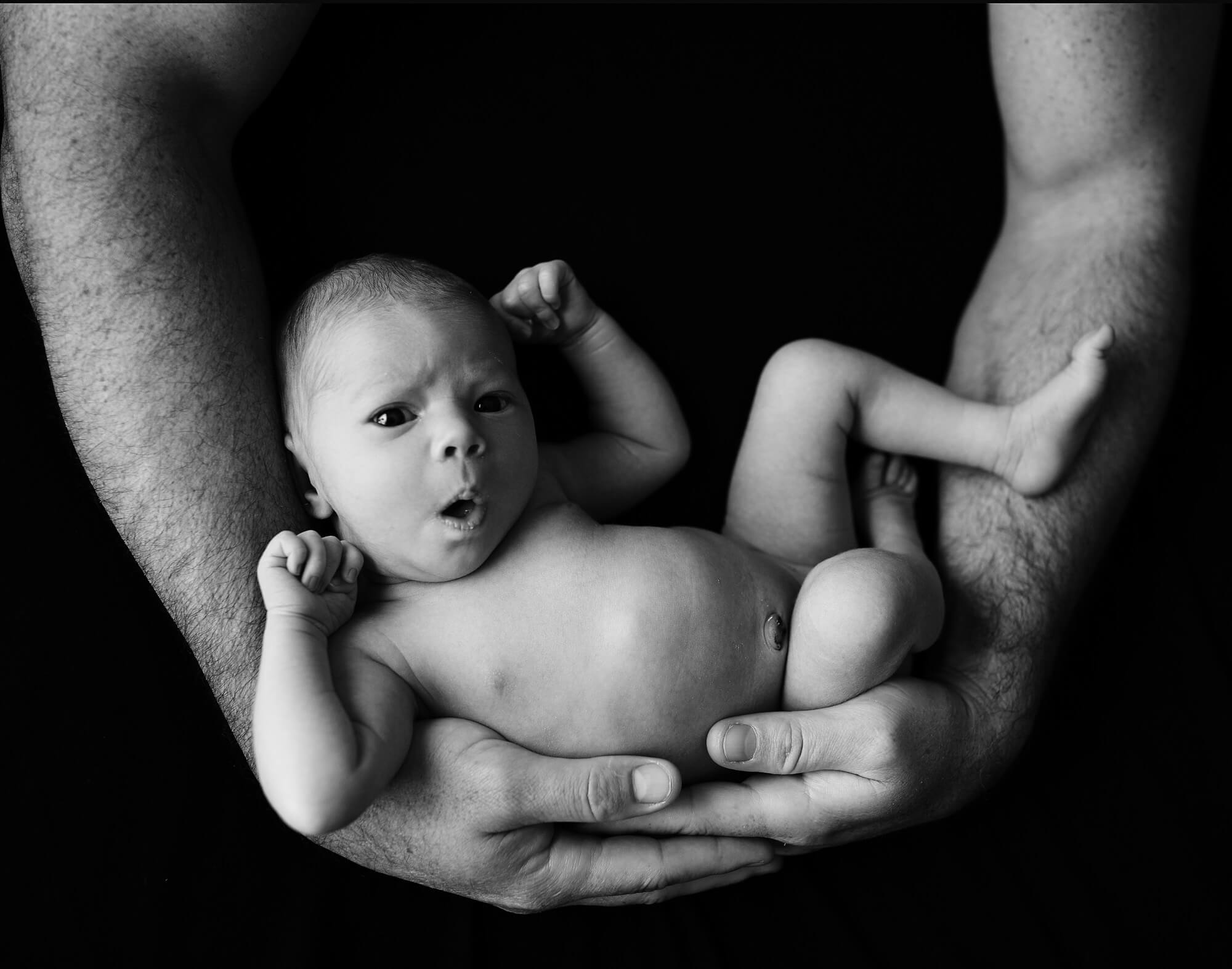 Black and white image of a newborn baby being held in her dads arms