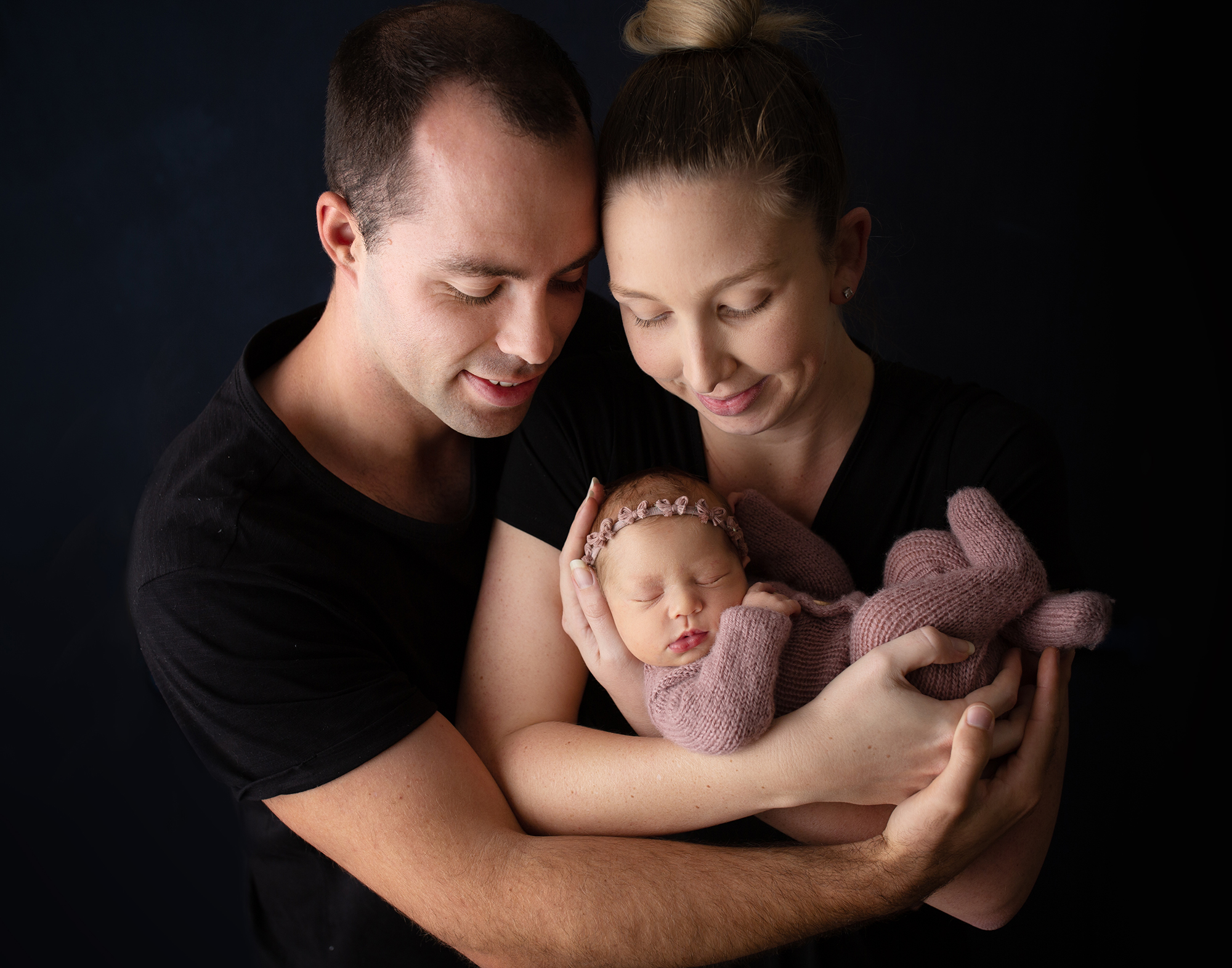 New parents mum, dad and newborn baby girl wearing a knitted dust pink romper in a studio photography session on the sunshine coast